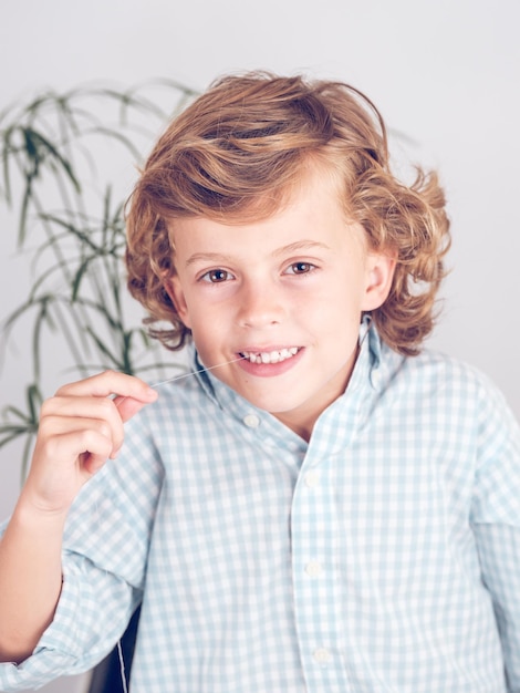 Photo adorable brave preteen boy with curly hair twitching out tooth with thread and looking at camera