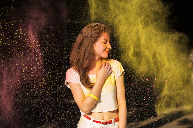 Adorable brunette model having fun in a cloud of yellow dry paint at Holi festival