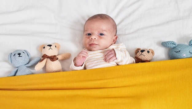 Adorable caucasian baby lying on bed with dolls at bedroom