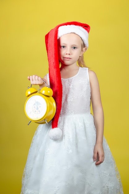 Adorable caucasian girl in christmas Santa hat with alarm clock in her hands