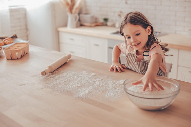 Adorable caucasian girl taking flour from the glass bowl on the kitchen