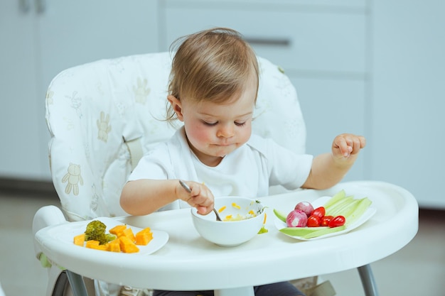 An adorable Caucasian toddler girl eats vegetables on her own pricking them with hands