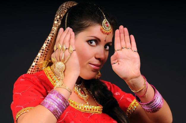 Adorable caucasian white adult woman in indian costume raises hands up. Female portrait on dark background