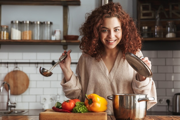adorable caucasian woman holding cooking ladle spoon while eating soup with fresh vegetables in kitchen at home