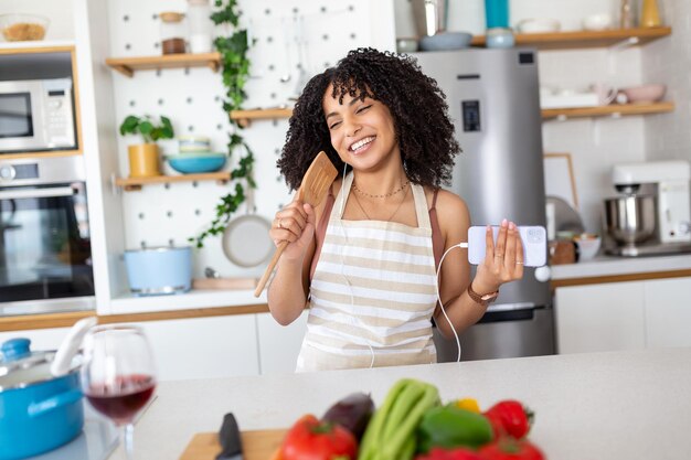 Adorable cheerful beautiful woman singing dancing with spoon and pan cover in modern light white kitchen cooking homemade breakfast dish with domestic products