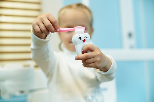 Adorabile bambino che pulisce un dente giocattolo bianco con uno spazzolino da denti nello studio dentistico.