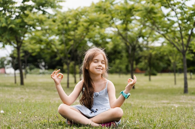 愛らしい子供の女の子が座って、公園で蓮華座で瞑想している子供たちのリラックスと瞑想屋外穏やかな幼児のライフスタイル人生を楽しむ
