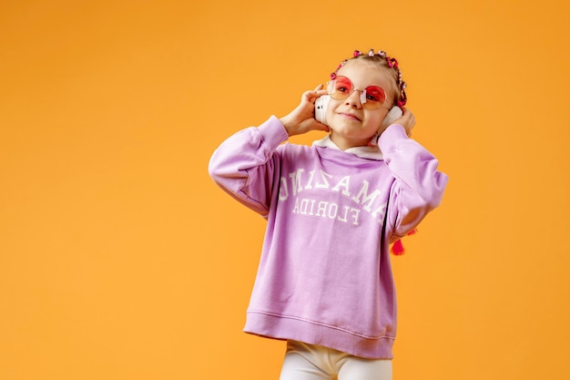 Adorable child in rounded glasses with pink dreadlocks listen to