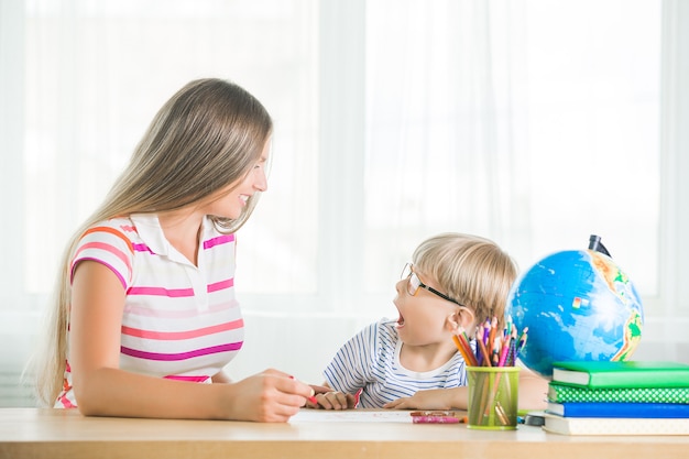 自宅で母親と一緒に勉強していたかわいい子。一緒に宿題をしている家族。息子が仕事を学ぶのを助ける若いお母さん。