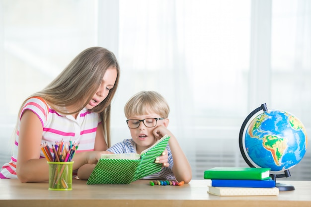 自宅で母親と一緒に勉強していたかわいい子。一緒に宿題をしている家族。息子が仕事を学ぶのを助ける若いお母さん。