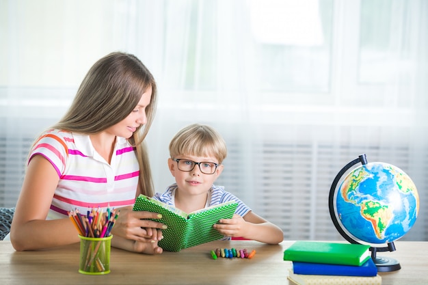 Adorable child studying with his mother at home. family doing\
homework together. young mom helping her son to learn a task.