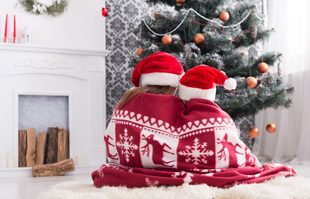 Adorable children in santa hats near christmas tree, wait for holiday gifts