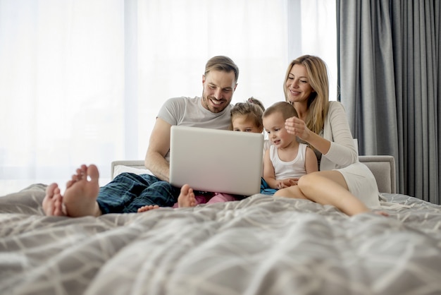 Adorable couple lying on the bed and watching something on the laptop with their children