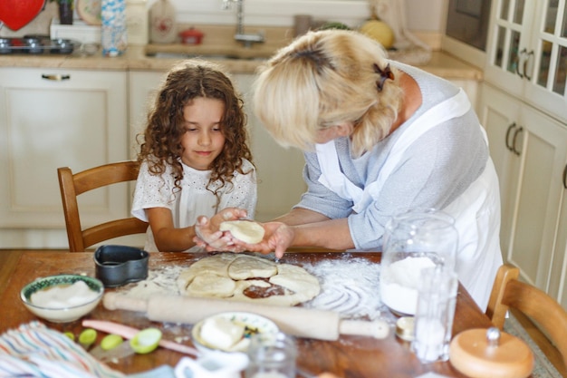 Adorable curly little girl with her grandmother cooking together at kitchen table. helps grandma in the kitchen.