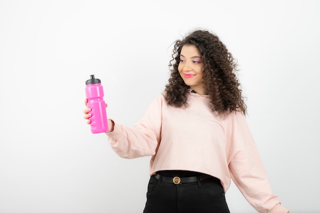 Adorable curly woman with pink water bottle standing over white.