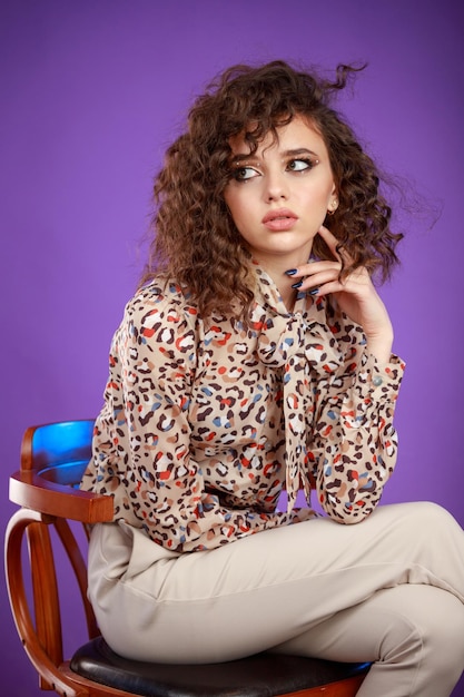 Adorable curlyhaired girl sitting on a chair on purple background High quality photo