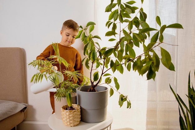 Adorable cute boy caring of indoor plants at home A little helper in the household leisure activity Child watering plants Home gardening concept Cozy room earth colors Casual clothing