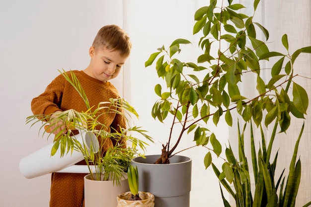 Adorable cute boy caring of indoor plants at home A little helper in the household leisure activity Child watering plants Home gardening concept Cozy room earth colors Casual clothing