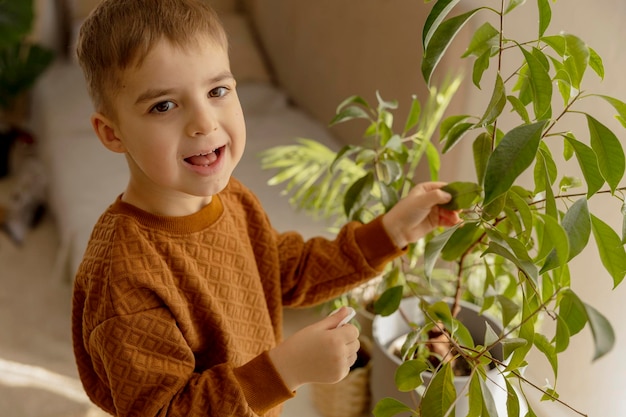 Photo adorable cute boy caring of indoor plants at home a little helper in the household