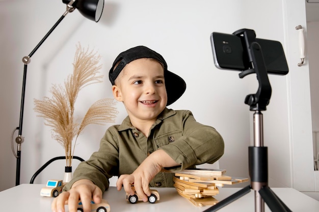 Adorable cute little boy blogger recording lifestyle blog talking to camera of smartphone on tripod Young influencer filming vlog for his channel Child makes video for his followers online