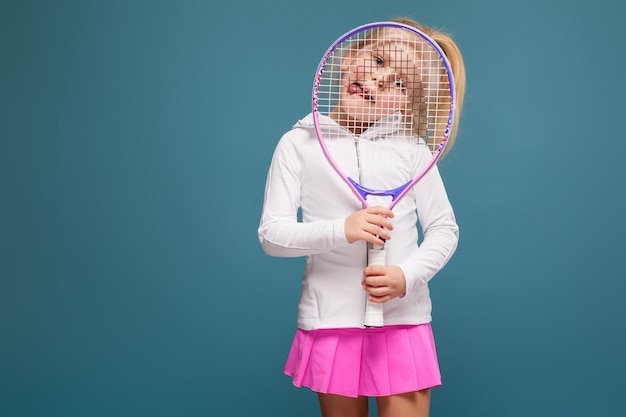 Фото Очаровательная милая маленькая девочка в белой рубашке, белой куртке и розовой юбке с теннисной ракеткой