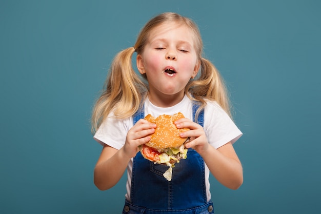 Adorable cute little girl in white shirt and jean jumpsuit with hamburger