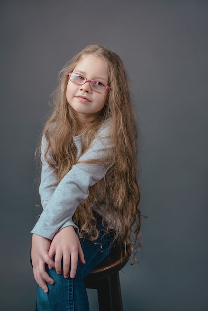 Adorabile bambina carina con lunghi capelli biondi con gli occhiali e in abiti casual in studio fotografico