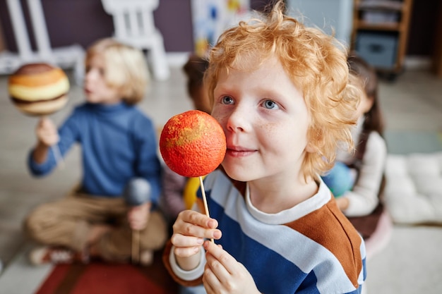 Adorable gingerhaired boy holding planet model of mars by his face while studying astronomy at lesso