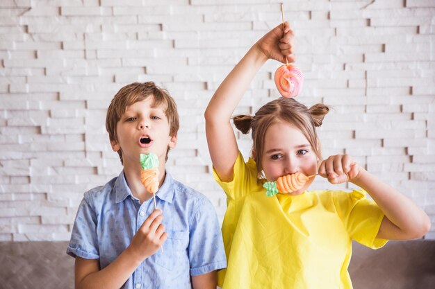 Adorable girl and boy holding colorful sweet meringues on a stick on Easter day