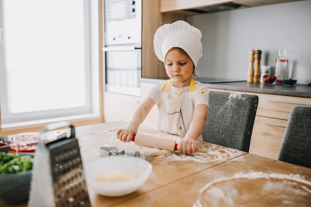 Adorable girl in chef hat and apron rolling out pastry dough