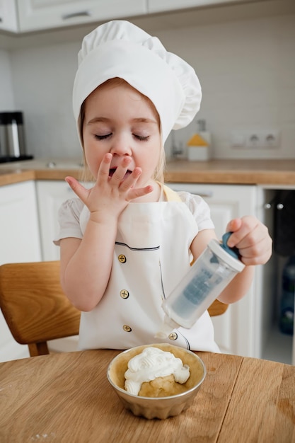 キッチンでケーキを準備するシェフの帽子とエプロンを着た愛らしい女の子