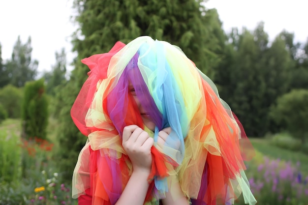 Adorable girl in colorful rainbow dress on her head playing outdoors