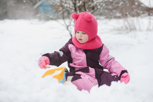 Adorable girl dig snow with shovel and pail on playground covered with snow little girl playing in winter outdoors