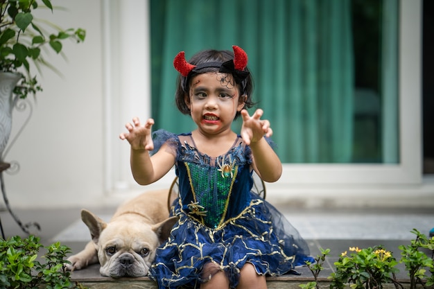 彼女の犬と一緒に屋外に座っているハロウィーンの衣装で愛らしい女の子