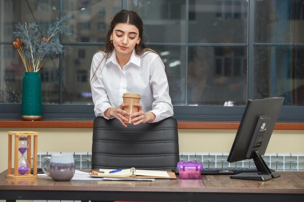 Ragazza adorabile che tiene una tazza di caffè e la guarda