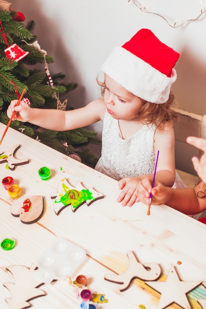 Adorable girl is painting wooden Christmas figurines