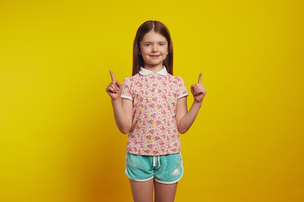 Adorable girl kid shows promo with joy points above with both index fingers