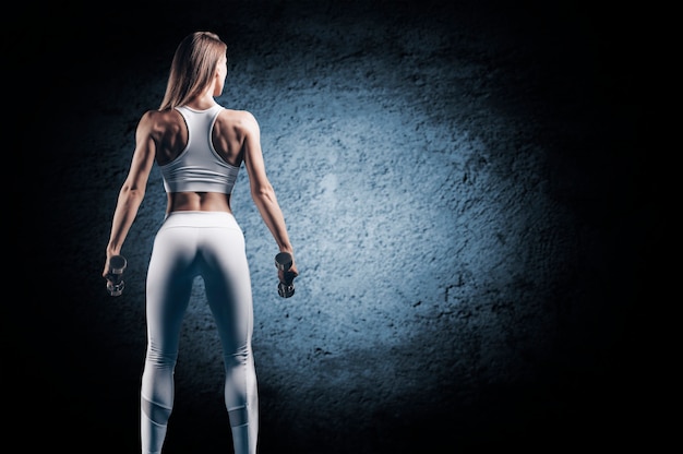 Adorable girl posing in the gym with dumbbells