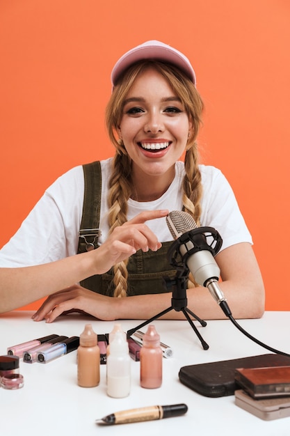 adorable girl recording blog broadcast with microphone about new cosmetic products isolated on orange wall