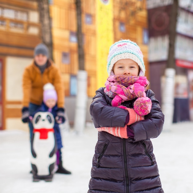 Adorable girl on skating rink, dad with little sister 