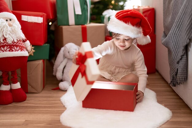 집에서 크리스마스 트리 옆에 앉아 선물을 풀고 있는 사랑스러운 소녀