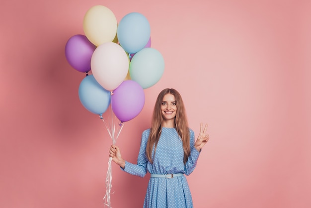 Adorable girl with many air balloons on pink background