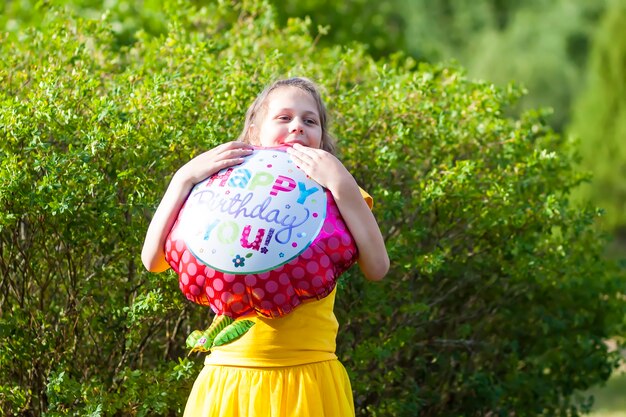 Adorabile ragazza in abito giallo con palloncino colorato festivo di buon compleanno a forma di fiore. bambino felice all'aperto