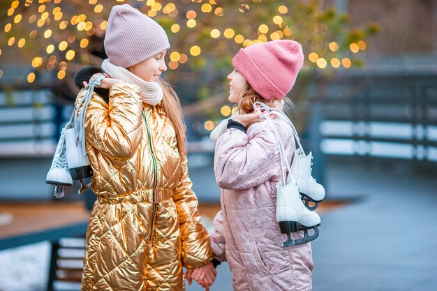 Adorable girls skating on ice rink outdoors in winter snow day