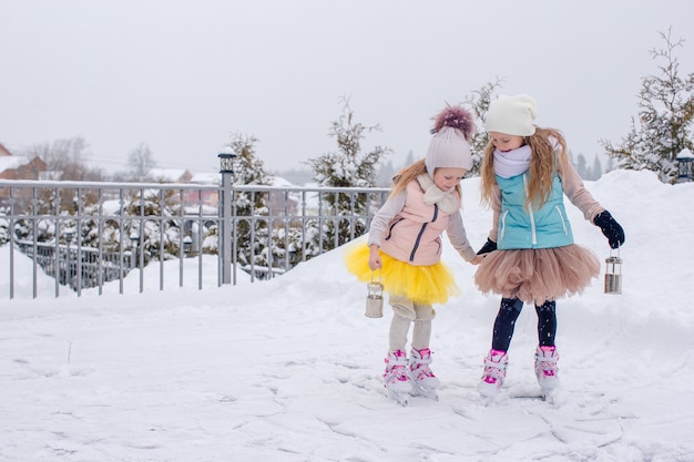 Ragazze adorabili che pattinano sulla pista di pattinaggio sul ghiaccio all'aperto nel giorno della neve di inverno