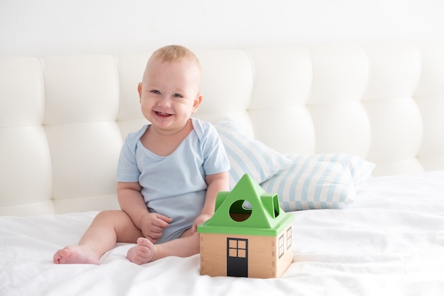 Photo adorable happy baby boy sits on bed and play with a toy sorter