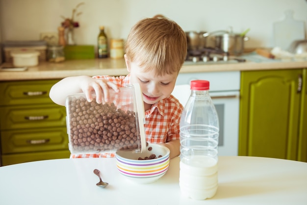 Adorable happy kid boy preparing breakfast or lunch chocolate cereal with milk