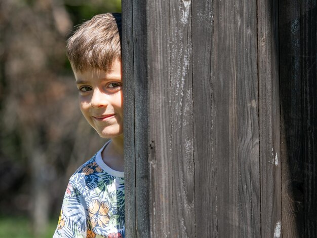 Adorable happy kid peeking around the tree playing hide and seek in a park at summer evening