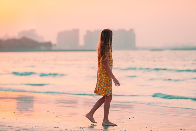 Adorable happy little girl on white beach at sunset.