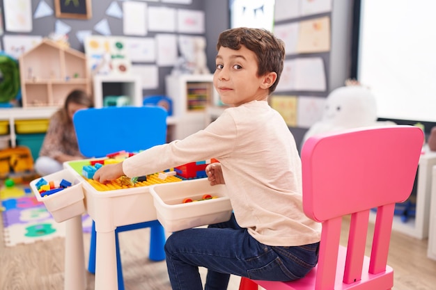 Adorable hispanic boy playing with construction blocks sitting on table at kindergarten